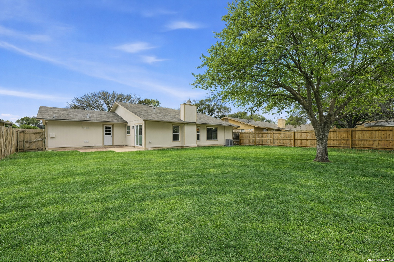 Backyard of 8247 Lewiston St with lush green lawn, mature oak tree, and wood privacy fence